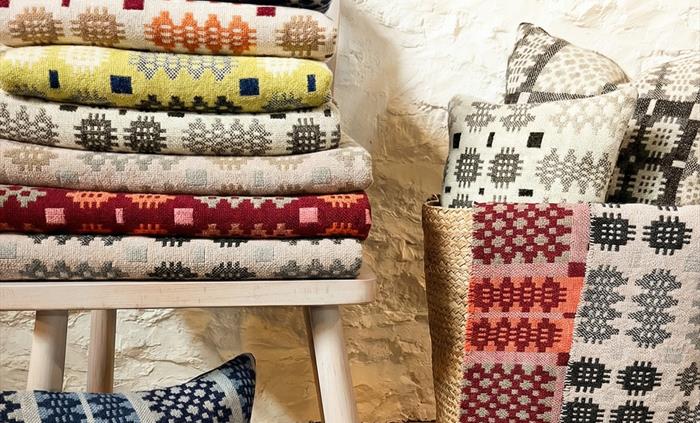 Woven blankets and cushions on display next to a white stone wall.